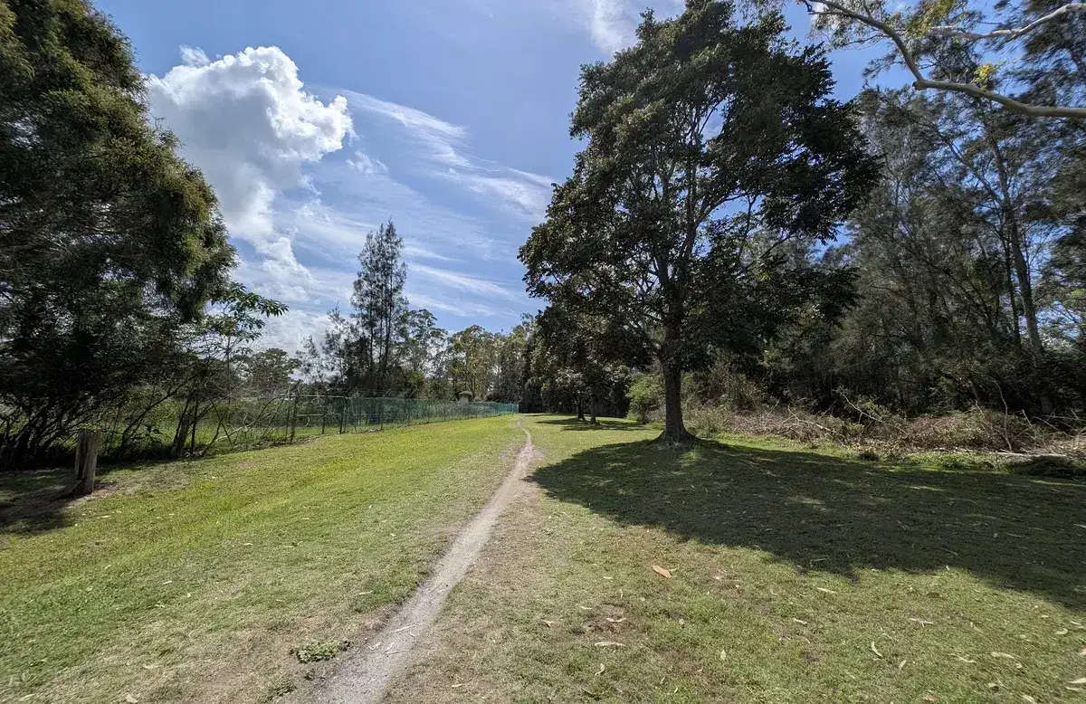 Dirt track crossing open grassland under a cloudy blue sky
