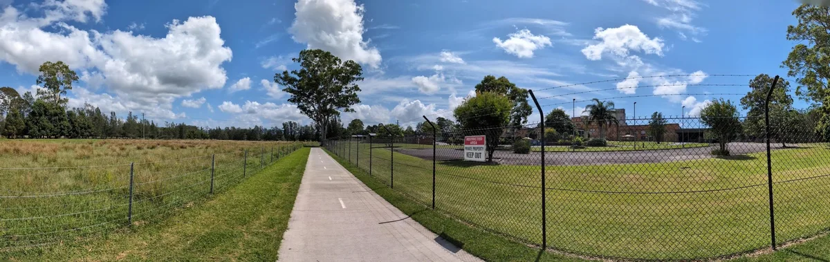 Paved shared path beside a fenced paddock with a keep out sign