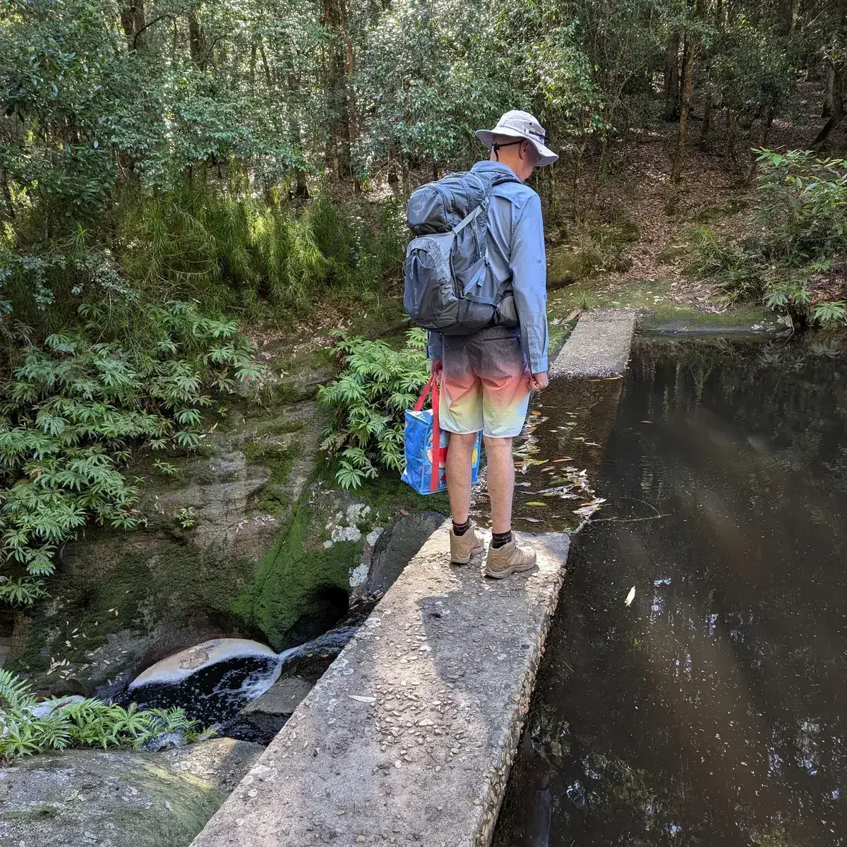 Hiker with a backpack pausing on the dam wall above the pool