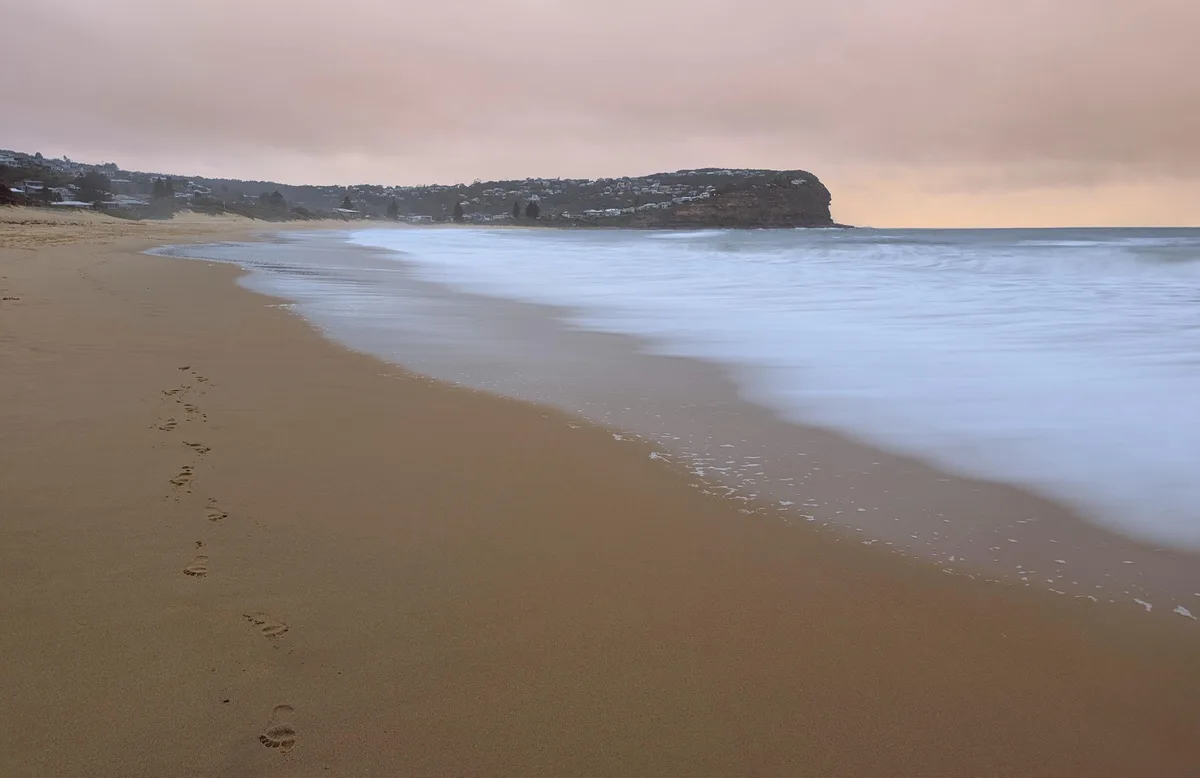 Footprints leading across the sand toward the surf at dusk
