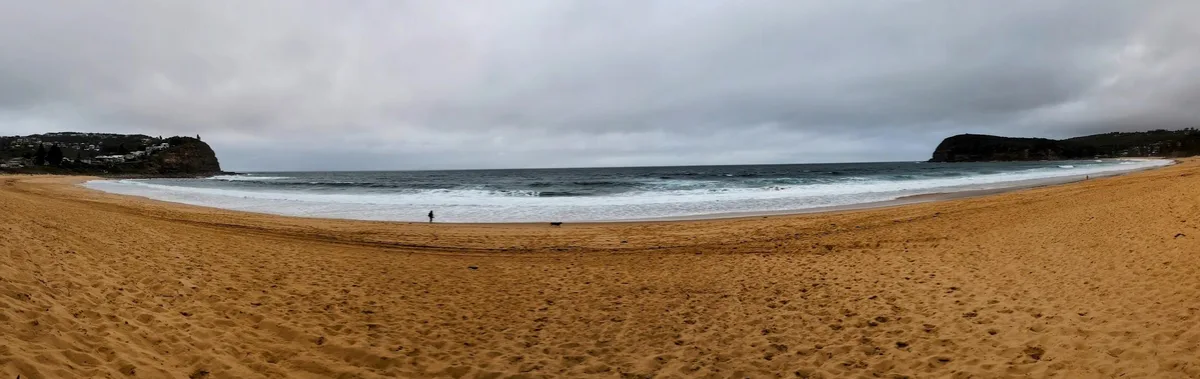 Lone walker on the shoreline beneath the cliffs at Copacabana