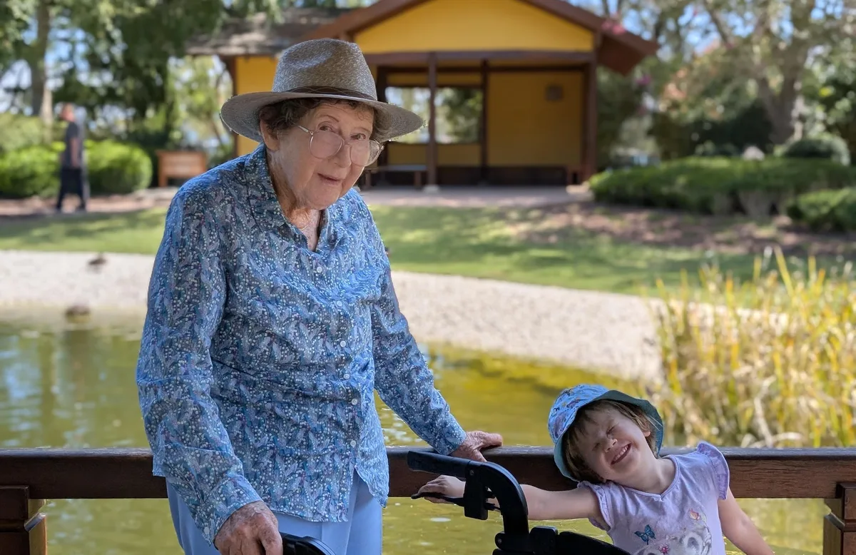 Woman in a sun hat pausing with a young child beside a garden pond