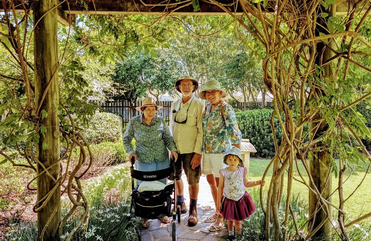 Family group standing under a wisteria covered pergola in the gardens