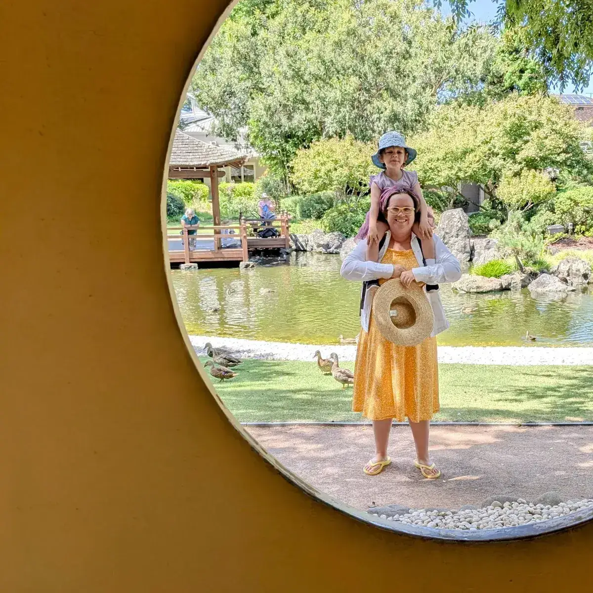Woman carrying a child on her shoulders framed by a circular yellow window