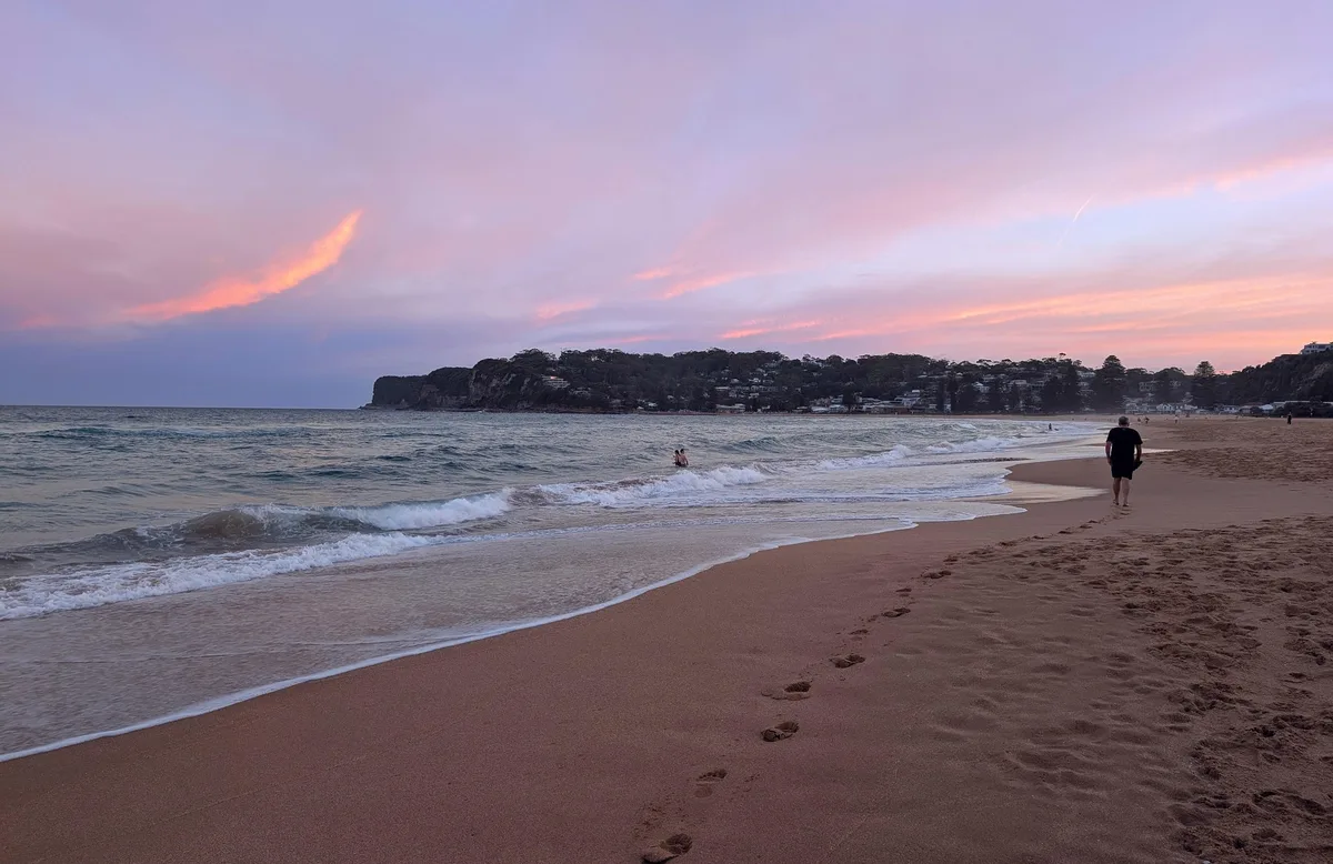 Solitary walker along the shoreline at North Avoca beach at sunset