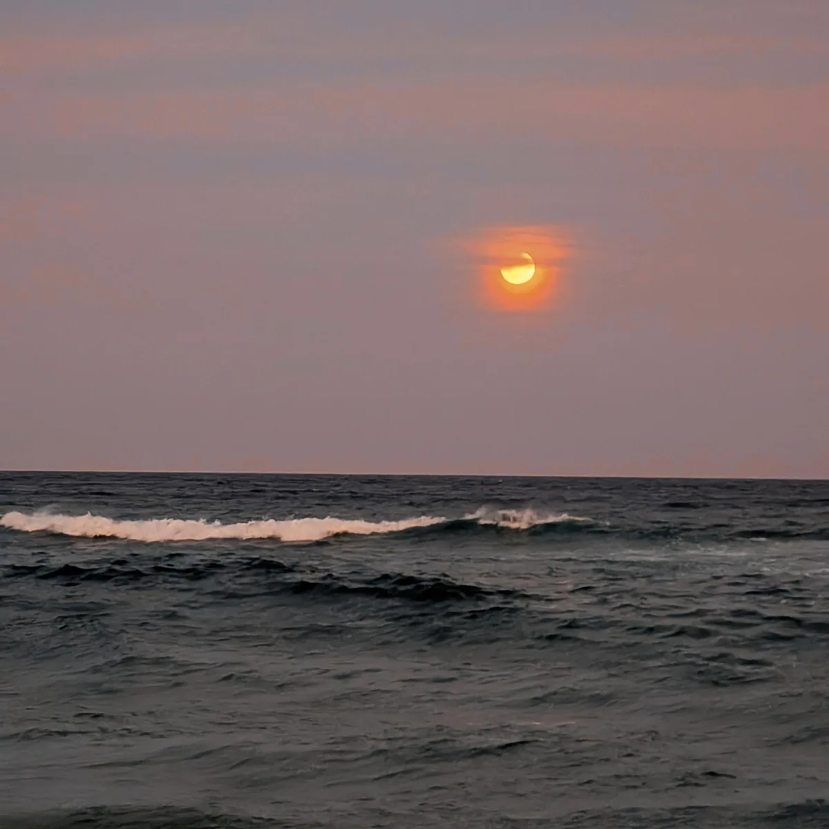 Crescent moon glowing orange over the ocean at North Avoca