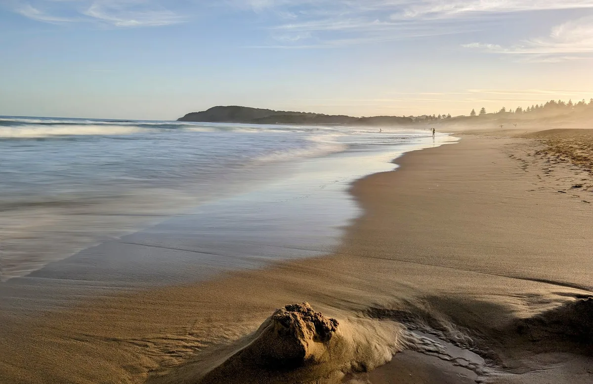 Sandy beach curving toward a headland with swimmers in the surf