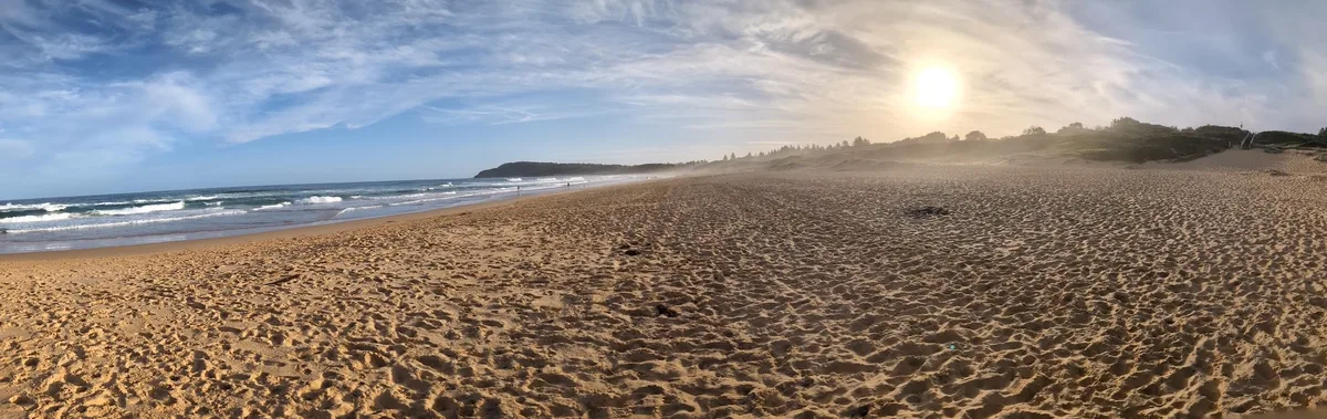 Wide panorama of an empty beach with footprints stretching toward a headland