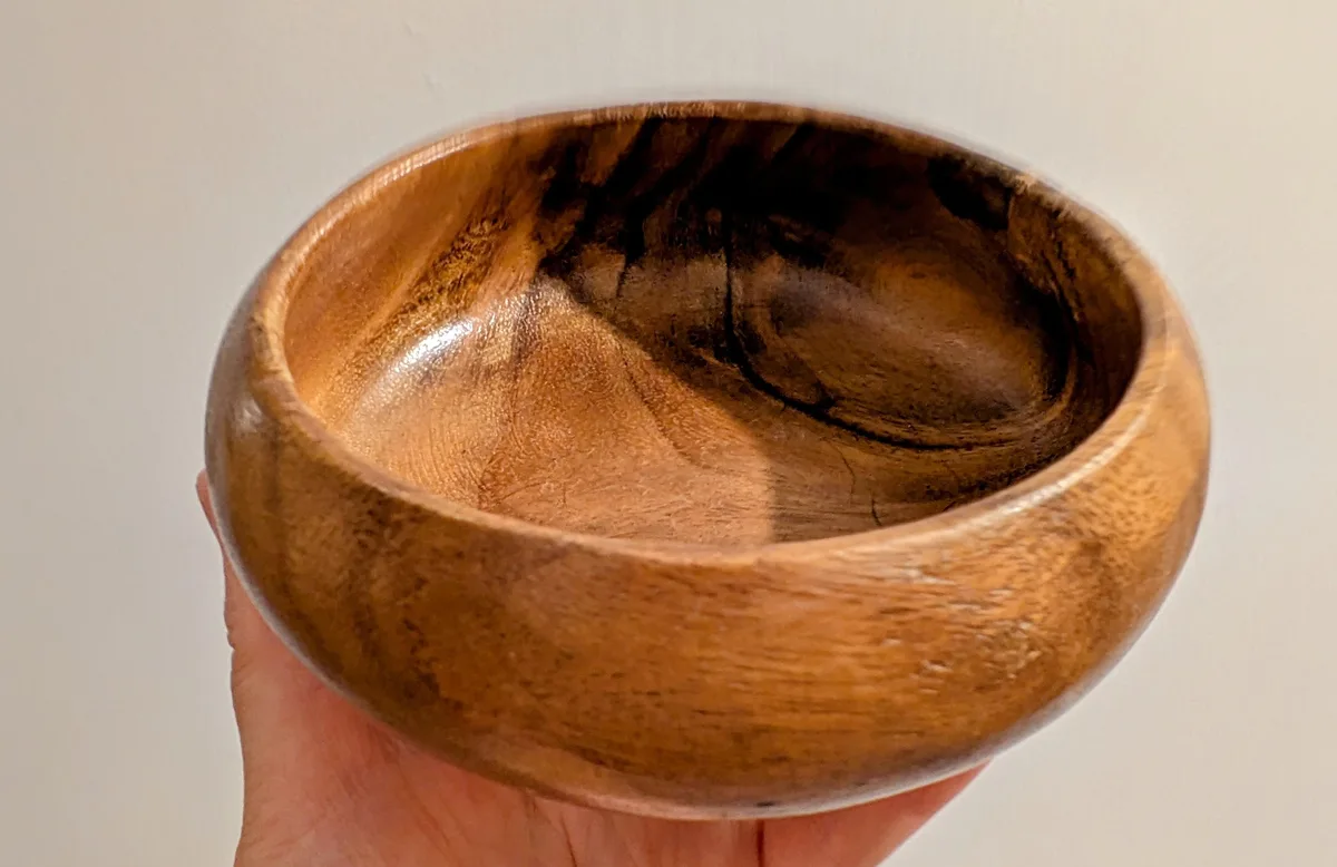 Hand holding a polished timber bowl with dark grain pattern