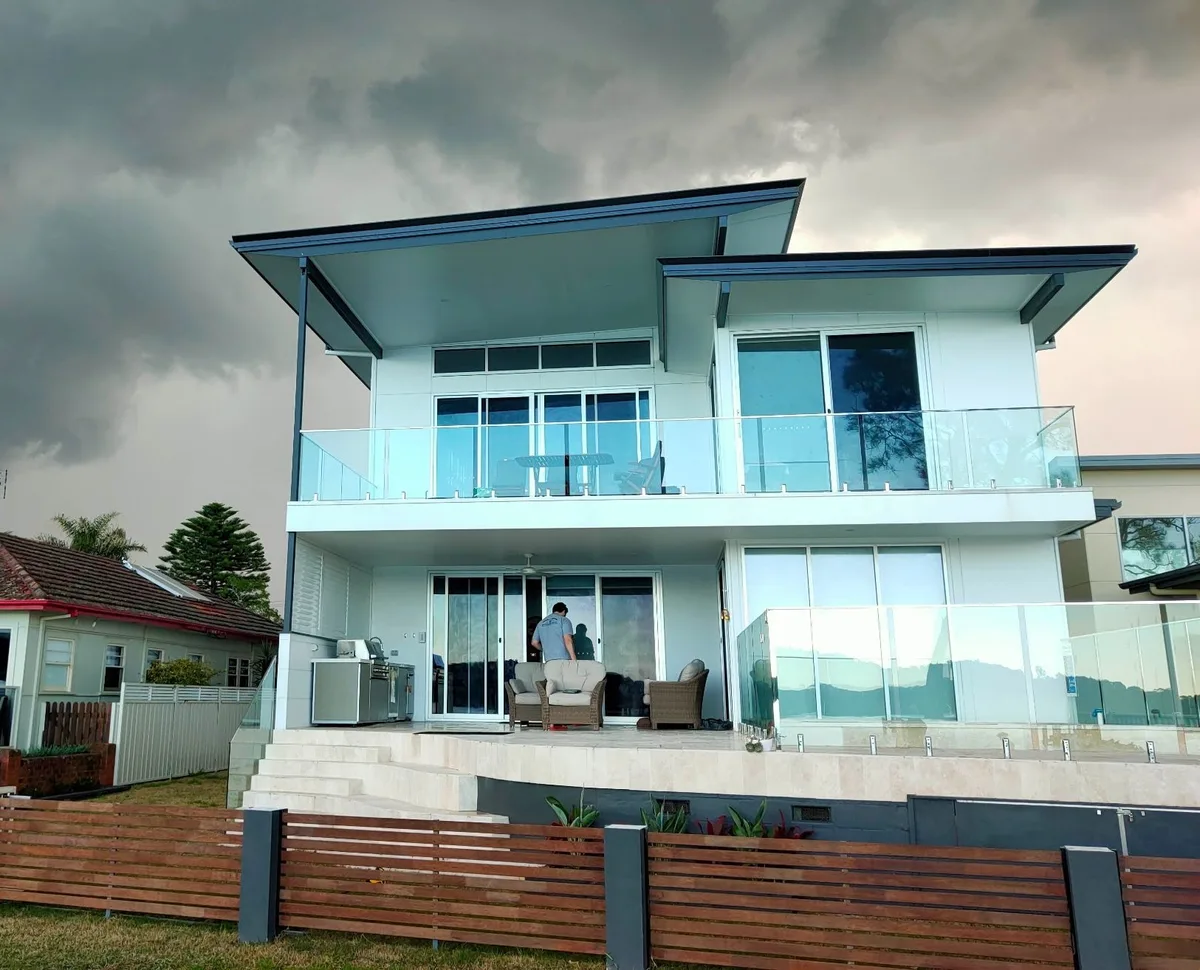 two storey glass balustraded home under a dark storm sky on the coast